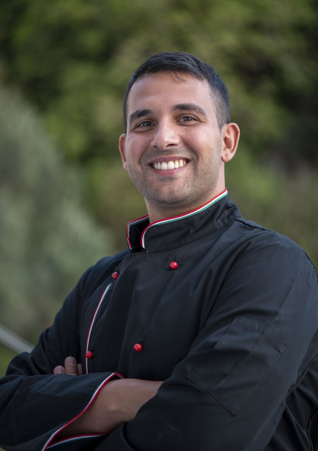 Alessandro Conte in giacca da chef nera, a braccia conserte all’aperto
